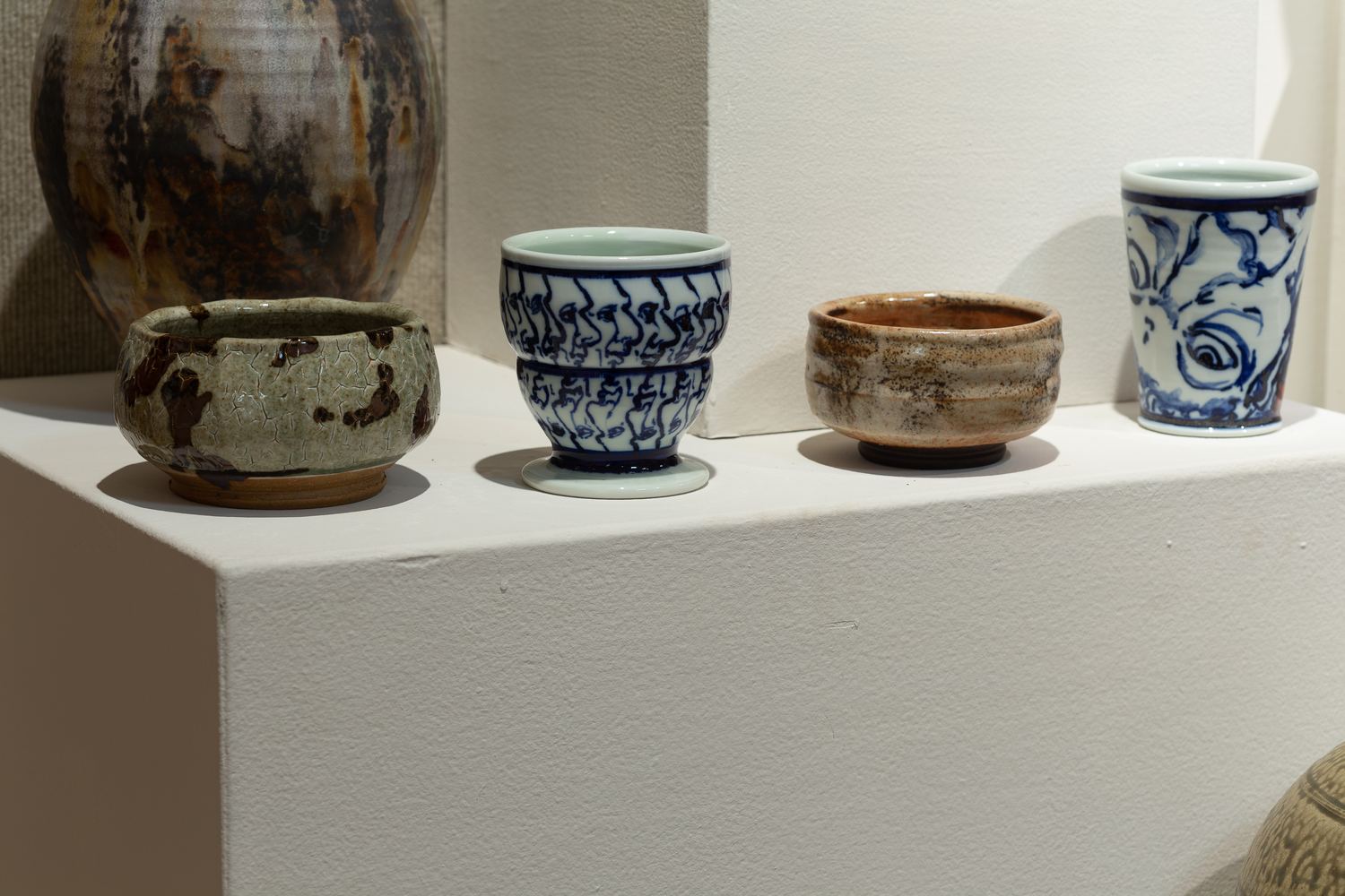 Keaton Wynn ceramics: cups, bowls and a blue-and-white beaker on a plinth